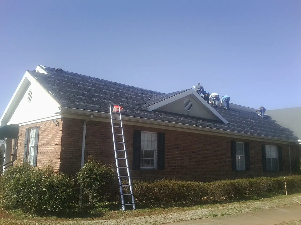 Crew tearing shingles off a brick ranch roof with a ladder set — Metal Roof Repair work by our crew in Salem