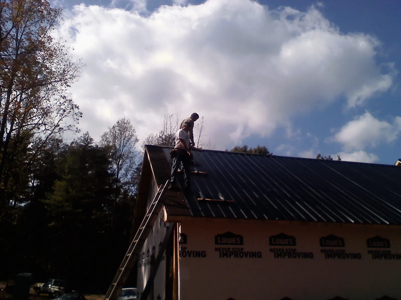 Roofer fastening dark metal panels high against a cloudy sky, from a Roof Inspection job in Salem